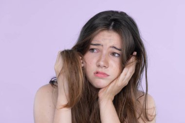 Beautiful girl feel sad, worry about her damaged hair with isolated background. Concept of dry lifeless hair. Young charming girl hold her tangled hair and look at it with worried expression.