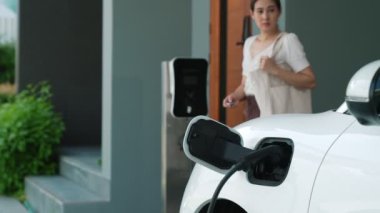 Evinde şarj edilen elektrikli bir araçla işten yeni dönen modern bir kadının ilerici yaşam tarzı. Elektrikli araç, sürdürülebilir temiz enerjiyle çalışıyor..