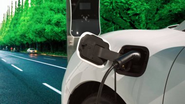 Çağdaş yeşil şehir ESG yeşil ağaçlar elektrikli araçla arka planda, EV araba şarj noktasındaki enerji yenilenebilir enerji taşımacılığıyla çevre bilincini artırmak için şarj ediliyor.