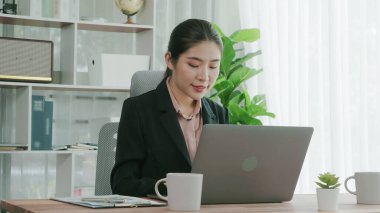 Ofiste çalışan ve dizüstü bilgisayar yazan hevesli bir iş kadını. Masasında oturmuş laptopla çalışan güzel bir ofis hanımı..