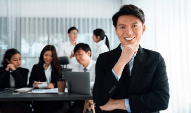 Portrait of focus young successful confident male manager, executive wearing business wear in harmony office arm crossed with blurred meeting background of colleagues, office worker.