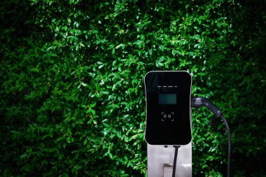 Charging station with greenery foliage background for combination of nature and alternative energy for progressive future renewable energy for electric car. Charger point with connecter device.