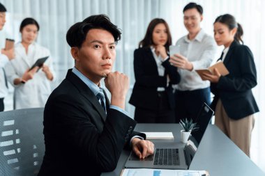 Portrait of focus young successful confident male manager, executive wearing business wear in harmony office arm crossed with blurred meeting background of colleagues, office worker.