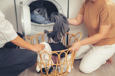 Senior couple working together to complete their household chores at the washing machine in a happy and contented manner. Husband and wife doing the usual tasks in the house.