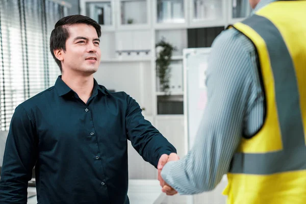 An engineer with a protective vest handshake with an investor in his office. Following a successful meeting, employee and employer form a partnership.