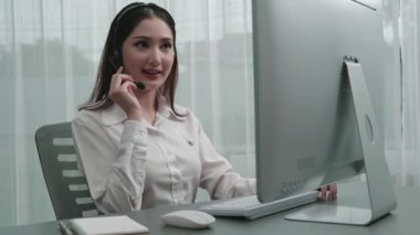 Masasında dizüstü bilgisayarla çalışan kulaklık ve mikrofon takan Asyalı müşteri destek operatörü. Hevesli kadın çalışanlar müşteri hizmetleri sunuyor, destekleyici çağrı merkezi temsilcisi müşterilere yardım ediyor.