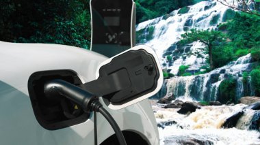 Elektrikli araba, doğal ortam, şelale ve akış arkaplanındaki şarj istasyonundan enerji yüklüyor. Yenilenebilir enerji kaynaklı EV otomobillerin enerji sürdürülebilirliği kavramı.