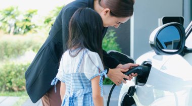 Evde şarj edilen elektrikli bir araçla okuldan yeni dönen anne ve kızın ilerici yaşam tarzı. Elektrikli araç, sürdürülebilir temiz enerjiyle çalışıyor..