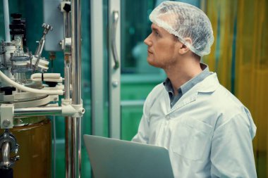CBD yağ çıkarıcısının yanında dizüstü bilgisayarla çalışan eczacı bilim adamı ve tıbbi esrar ürünleri üretmek için kullanılan bilimsel bir makine.