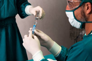 Cerrah şırıngayı steril ameliyat odasındaki cerrahi prosedür için tıbbi şişeden doldurdu. Doktor ve tıbbi personel ameliyat için tam koruma altında. Anestezi enjeksiyonunu hazırlayın.