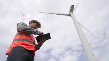 Gökyüzü arka planına sahip bir rüzgar türbini üzerinde çalışan mühendis. Yenilenebilir ve sürdürülebilir enerjinin gelecekteki üretimi için yenilikçi bir ideal. Rüzgar türbininden enerji üretimi.