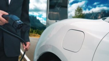 İş dünyasındaki yenilikçi adam elektrikli arabasını dağlarla dolu bir kırsal kesimdeki şarj istasyonundan alıyor. Yol yolculuğu, EV arabalı macera yenilenebilir enerjiyle çalışıyor..