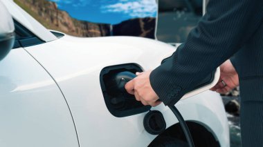 İlerici adam arka planda kırsal dağ olan şarj istasyonundan elektrik kablosu yerleştiriyor. Temiz ortam için elektro motor tarafından kullanılan EV otomobil