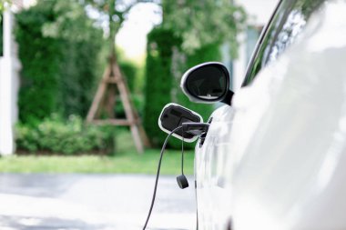 Closeup electric vehicle plugged-in with cable from charging point powered for progressive concept by alternative clean energy rechargeable EV car at home charging station.