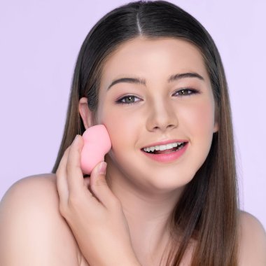 Facial cosmetic makeup concept. Portrait of young charming girl applying dry powder foundation. Beautiful girl smiling with perfect skin putting cosmetic makeup on her face.