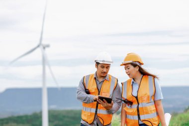 Erkek ve kadın mühendisler kırsal kesimdeki bir tepenin tepesinde ya da dağda rüzgar çiftliğinde çalışıyorlar. Yenilenebilir ve sürdürülebilir enerjinin gelecekteki üretimi için yenilikçi idealler.