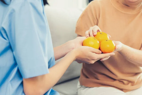 Young Caregiver Handing Oranges Her Contented Senior Patient Living Room — Foto Stock