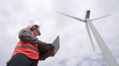 Gökyüzü arka planına sahip bir rüzgar türbini üzerinde çalışan mühendis. Yenilenebilir ve sürdürülebilir enerjinin gelecekteki üretimi için yenilikçi bir ideal. Rüzgar türbininden enerji üretimi.