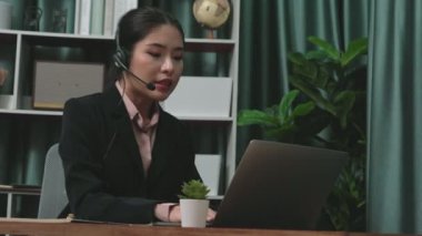 Kulaklık ve mikrofon takan iş kadını masasında çalışıyor ve dizüstü bilgisayar kullanıyor. Uzaktan kumandalı online toplantı için dizüstü bilgisayar kullanan hevesli kadın çalışanlar, ofiste iş videosu konferansı.