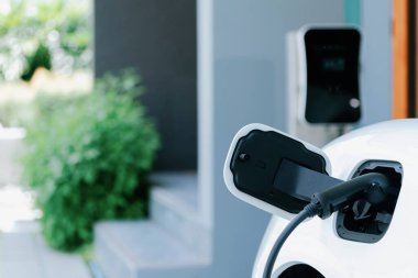 Closeup electric vehicle plugged-in with cable from charging point powered for progressive concept by alternative clean energy rechargeable EV car at home charging station.