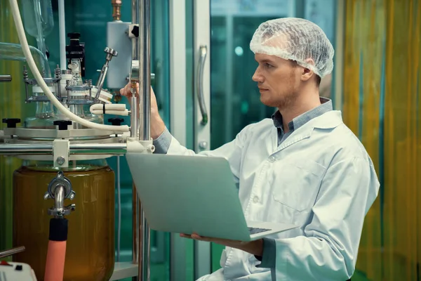 Cbd油抽出器の近くでラップトップを扱う薬局の科学者と 薬用大麻製品を作成するために使用される科学機械 — ストック写真