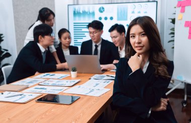 Focus portrait of female manger, businesswoman in the harmony meeting room with blurred of colleagues working together, analyzing financial paper report and dashboard data on screen in background.