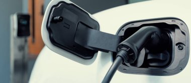 Closeup electric vehicle plugged-in with cable from charging point powered for progressive concept by alternative clean energy rechargeable EV car at home charging station.