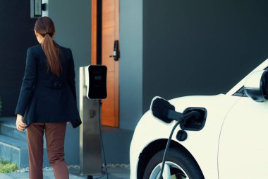 Progressive woman install cable plug to her electric car with home charging station. Concept of the use of electric vehicles in a progressive lifestyle contributes to clean environment.