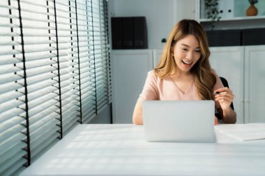 A young Asian female employee sitting at her desk in her office, sitting at desktop in workstation.