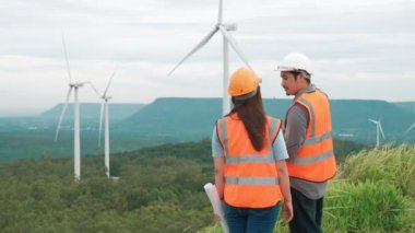 Erkek ve kadın mühendisler kırsal kesimdeki bir tepenin tepesinde ya da dağda rüzgar çiftliğinde çalışıyorlar. Yenilenebilir ve sürdürülebilir enerjinin gelecekteki üretimi için yenilikçi idealler.