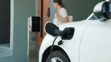 Bir kadın evinde elektrikli araç şarj aletinin fişini çekiyor. İlerici bir yaşam tarzında elektrikli araçların kullanımı, temiz ve sağlıklı bir çevreye katkıda bulunur..