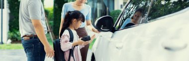 Progressive young happy family with electric vehicle and home backyard charging station. Green and clean energy from electric vehicles for healthy environment. Eco power from renewable source.