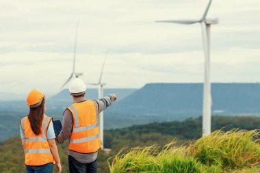 Erkek ve kadın mühendisler kırsal kesimdeki bir tepenin tepesinde ya da dağda rüzgar çiftliğinde çalışıyorlar. Yenilenebilir ve sürdürülebilir enerjinin gelecekteki üretimi için yenilikçi idealler.