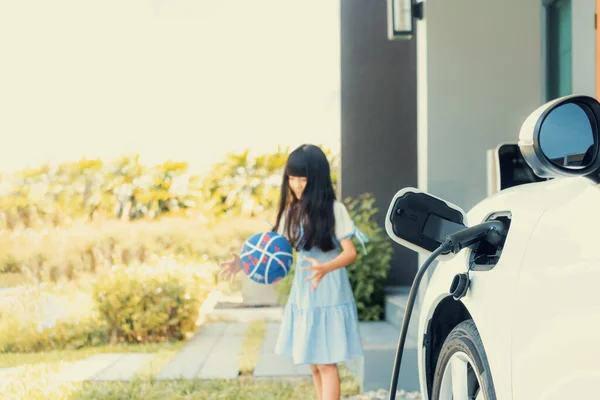 Focus home electric charging station for electric vehicle as alternative clean sustainable energy technology concept with blurred progressive young girl playing in the background at her home.