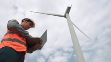 Gökyüzü arka planına sahip bir rüzgar türbini üzerinde çalışan mühendis. Yenilenebilir ve sürdürülebilir enerjinin gelecekteki üretimi için yenilikçi bir ideal. Rüzgar türbininden enerji üretimi.