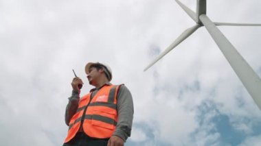 Gökyüzü arka planına sahip bir rüzgar türbini üzerinde çalışan mühendis. Yenilenebilir ve sürdürülebilir enerjinin gelecekteki üretimi için yenilikçi bir ideal. Rüzgar türbininden enerji üretimi.