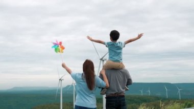 İlerici mutlu aile kavramı rüzgâr türbini çiftliğinde eğleniyor. Rüzgar türbini jeneratörüyle gelen elektrik jeneratörü kırsal bölgede tepe ve ufukta dağ var..