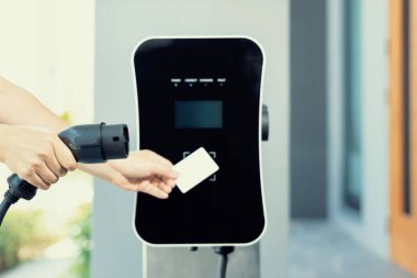 Hand holding credit card to pay public charging station and recharge her electric vehicle, symbolizing progressive lifestyle, combines e-wallet technology and sustainable transportation option.