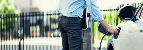 stock image Closeup progressive man holding EV charger plug from public charging station for electric vehicle with background of residential building as concept eco-friendly sustainability energy car concept.