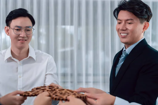 stock image Closeup hand holding wooden gear by businesspeople wearing suit for harmony synergy in office workplace concept. Group of people hand making chain of gears into collective form for unity symbol.