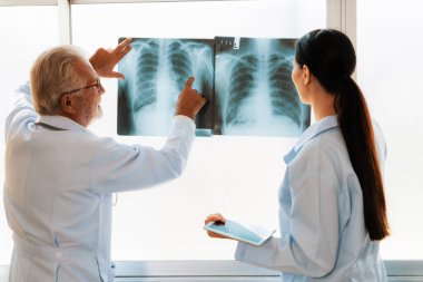 Hastane steril odasında, iki profesyonel radyolog tıbbi röntgen teşhisi için bir radyografı tutuyor ve inceliyor. Acemi doktor tecrübeli yaşlı doktordan hasta durumuyla ilgili tavsiye ister..
