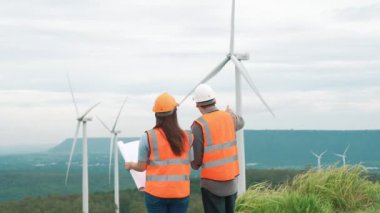 Erkek ve kadın mühendisler kırsal kesimdeki bir tepenin tepesinde ya da dağda rüzgar çiftliğinde çalışıyorlar. Yenilenebilir ve sürdürülebilir enerjinin gelecekteki üretimi için yenilikçi idealler.