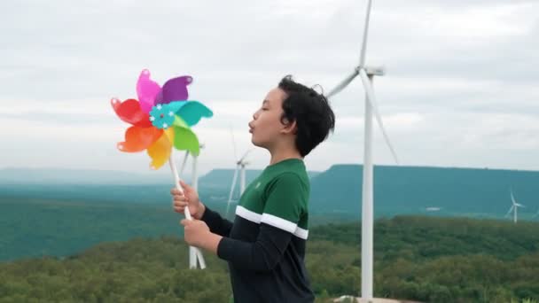丘の上の風力タービン農場 緑のフィールドで風力タービンのおもちゃで遊んで進歩的な若いアジアの少年 再生可能エネルギー発電からのグリーンエネルギー — ストック動画
