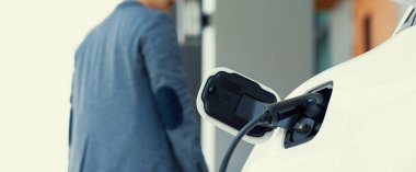 Focus electric car charging at home charging station with blurred progressive man walking in the background. Electric car using renewable clean for eco-friendly concept.