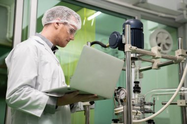 Eczacı bilimadamı CBD yağ çıkarıcısından bilgi kaydetmek için dizüstü bilgisayar ve tıbbi esrar ürünleri üretmek için kullanılan bilimsel bir makine kullanıyor..