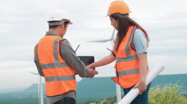 Erkek ve kadın mühendisler kırsal kesimdeki bir tepenin tepesinde ya da dağda rüzgar çiftliğinde çalışıyorlar. Yenilenebilir ve sürdürülebilir enerjinin gelecekteki üretimi için yenilikçi idealler.
