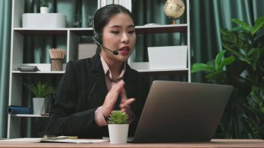 Masasında dizüstü bilgisayarla çalışan kulaklık ve mikrofon takan Asyalı müşteri destek operatörü. Hevesli kadın çalışanlar müşteri hizmetleri sunuyor, destekleyici çağrı merkezi temsilcisi müşterilere yardım ediyor.