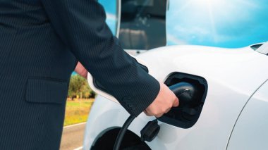 İlerici adam, yeşil çevre için yenilenebilir ve temiz enerjiyle çalışan EV otomobili hedefine ulaşmadan önce uzak bölgedeki şarj istasyonundan enerjiyi şarj etmek için duruyor.