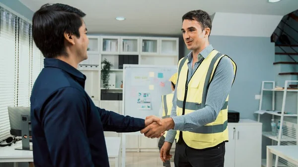 An engineer with a protective vest handshake with an investor in his office. Following a successful meeting, employee and employer form a partnership.