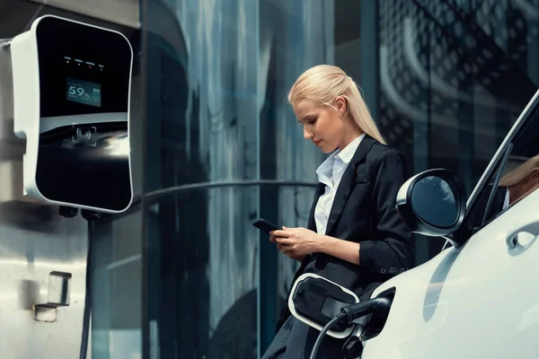 Businesswoman Wearing Black Suit Using Smartphone Leaning Electric Car Recharge — Φωτογραφία Αρχείου